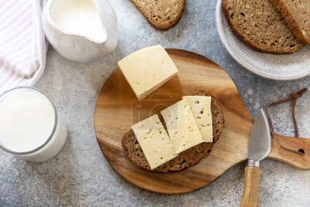Téléchargez les photos : Concept d'aliments sains, petit déjeuner, superaliments. Verre de lait d'amande et pain frais à grains entiers avec fromage sur table en pierre. - en image libre de droit