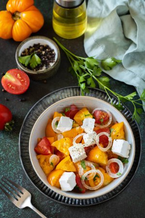 Photo for The concept of vegan or diet food. Tomato salad made from a mix of red and yellow tomatoes and feta cheese on a stone tabletop. - Royalty Free Image