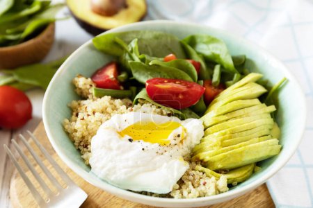 Photo for Keto diet. Delicious breakfast or brunch - poached egg, quinoa, avocado and fresh vegetable salad on the kitchen table. - Royalty Free Image