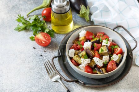 Healthy vegetarian diet food. Salad with grill eggplants, tomatoes and feta cheese on a gray stone tabletop. Copy space.