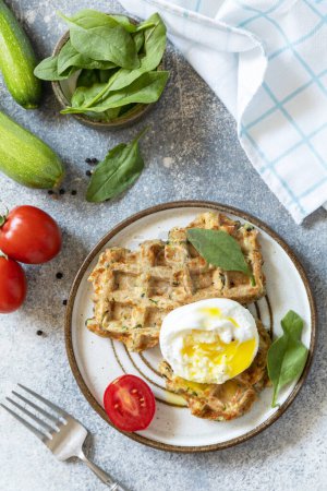 Das Konzept der diätetischen und gesunden Frühstück. Spinat und Zucchini vegane Waffeln mit pochiertem Ei auf einer Steinplatte. Blick von oben. Kopierraum.
