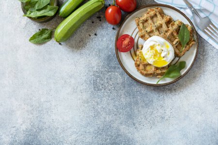 Photo for Spinach and zucchini vegan waffles with a poached egg on a stone tabletop. The concept of dietary and healthy breakfast. View from above. Copy space. - Royalty Free Image