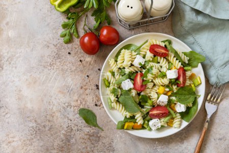 Photo for Salad with gluten free pasta, spinach, tomatoes, beans and feta cheese on a stone table. Italian food. Healthy food, vegetarian appetizer. View from above. - Royalty Free Image