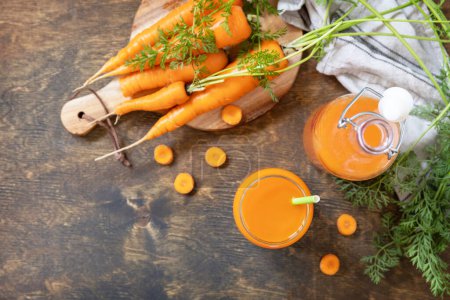 Photo for Fresh natural juice, healthy food concept. Glass jar of fresh carrot juice with fresh carrots on a rustic table. View from above. Copy space. - Royalty Free Image