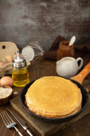Foto de Celebrating Pancake day, cooking healthy breakfast. Delicious homemade crepes or pancakes in a frying pan and ingredients on a rustic table. Copy space. - Imagen libre de derechos
