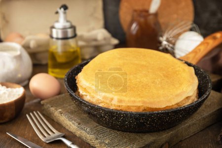 Foto de Celebrating Pancake day, cooking healthy breakfast. Delicious homemade crepes or pancakes in a frying pan and ingredients on a rustic table. - Imagen libre de derechos