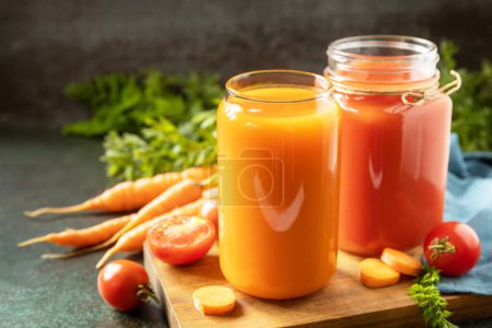 Foto de Tomate y jugo de zanahoria en vasos y tomates frescos en una mesa de piedra. Las vitaminas beben jugo de zanahoria y tomate, estilo de vida saludable. Copiar espacio. - Imagen libre de derechos