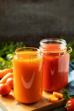 Foto de Las vitaminas beben jugo de zanahoria y tomate, estilo de vida saludable. Tomate y jugo de zanahoria en vasos y tomates frescos en una mesa de piedra. Copiar espacio. - Imagen libre de derechos