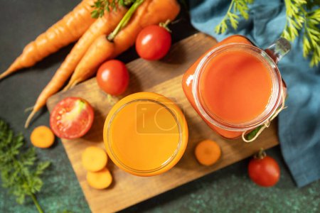 Foto de Tomate y jugo de zanahoria en vasos y tomates frescos en una mesa de piedra. Las vitaminas beben jugo de zanahoria y tomate, estilo de vida saludable. Vista desde arriba. - Imagen libre de derechos