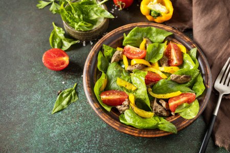 Photo for Warm salad from the baby spinach, chicken liver, tomatoes and peppers with spices and balsamic on stone background. Copy space. - Royalty Free Image