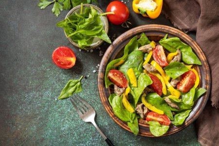 Photo for Warm salad from the baby spinach, chicken liver, tomatoes and peppers with spices and balsamic on stone background. View from above. Copy space. - Royalty Free Image