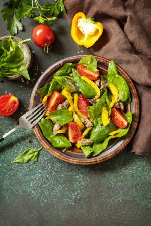 Photo for Warm salad from the baby spinach, chicken liver, tomatoes and peppers with spices and balsamic on stone background. View from above. Copy space. - Royalty Free Image