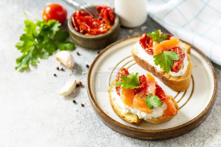 Photo for Open sandwiches or bruschetta with salted salmon, cheese and sun dried tomato on a stone table. Healthy food, seafood. Copy space. - Royalty Free Image