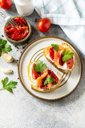 Foto de Abra sándwiches o bruschetta con salmón salado, queso y tomate secado al sol en una mesa de piedra. Comida saludable, mariscos. - Imagen libre de derechos