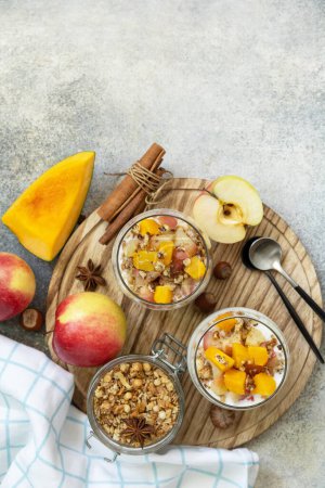 Photo for Healthy autumn or winter breakfast granola. Homemade dessert with yogurt, granola, caramel apples and pumpkin, cinnamon, nuts on a stone table. View from above. Copy space. - Royalty Free Image