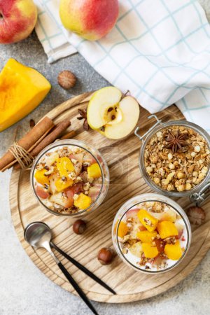 Photo for Healthy autumn or winter breakfast granola. Homemade dessert with yogurt, granola, caramel apples and pumpkin, cinnamon, nuts on a stone table. View from above. - Royalty Free Image