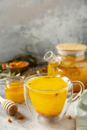 Téléchargez les photos : L'argousier et une tasse de thé d'argousier sain avec du miel sur une table en pierre. - en image libre de droit
