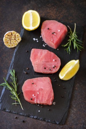 Photo for Seafood. Raw juicy tuna steaks  with spices and rosemary on a stone table. - Royalty Free Image