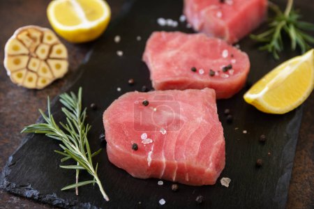Téléchargez les photos : Fruits de mer. Steaks de thon cru juteux aux épices et romarin sur une table en pierre. - en image libre de droit