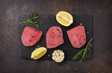 Photo for Seafood. Raw juicy tuna steaks  with spices and rosemary on a stone table. View from above. - Royalty Free Image