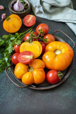 Téléchargez les photos : Diverses tomates colorées et feuilles de persil sur un fond de pierre sombre. De la nourriture biologique. Espace de copie. - en image libre de droit