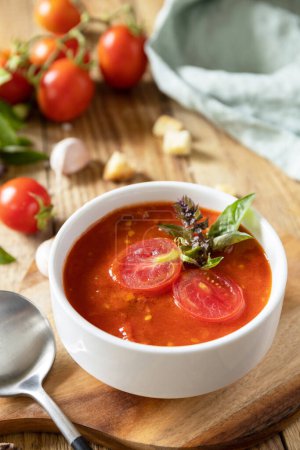 Foto de Sopa vegana puré de tomates. Dieta saludable baja en carbohidratos. Cuenco de sopa de crema de tomate con albahaca y croutons en una mesa rústica. - Imagen libre de derechos