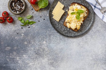 Photo for Scrambled eggs on whole grain bread on a stone table. Homemade breakfast or brunch meal - scrambled eggs. View from above. Copy space. - Royalty Free Image