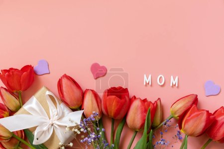 Caja de regalo con lazos pequeños corazones y tulipanes rojos sobre fondo rosa pastel con espacio vacío. Concepto de celebración del Día de la Madre. Vista desde arriba.