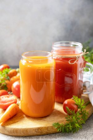 Foto de Tomate y jugo de zanahoria en vasos sobre una mesa de piedra. Las vitaminas beben jugo de zanahoria y tomate. Estilo de vida saludable. Copiar espacio. - Imagen libre de derechos