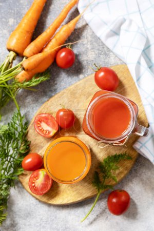 Foto de Las vitaminas beben jugo de zanahoria y tomate. Tomate y jugo de zanahoria en vasos sobre una mesa de piedra. Estilo de vida saludable. Vista desde arriba. - Imagen libre de derechos