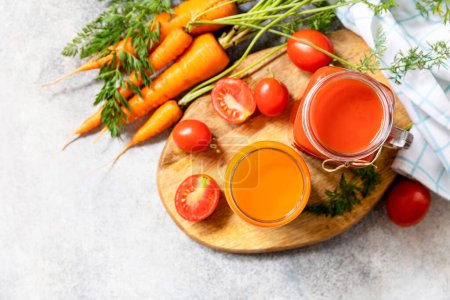 Foto de Tomate y jugo de zanahoria en vasos sobre una mesa de piedra. Las vitaminas beben jugo de zanahoria y tomate. Estilo de vida saludable. Vista desde arriba. Copiar espacio. - Imagen libre de derechos