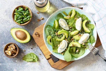Photo for Organic green avocado and spinach salad with eggs, green beans, nuts on a stone table. Healthy food, summer healthy eating. View from above. - Royalty Free Image