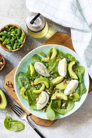Photo for Healthy food, summer healthy eating. Organic green avocado and spinach salad with eggs, green beans, nuts on a stone table. View from above. - Royalty Free Image
