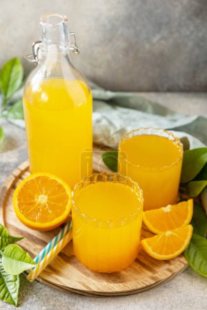 Foto de Naranjas maduras y dos vasos de jugo de naranja recién exprimido en una mesa de piedra. Copiar espacio. - Imagen libre de derechos
