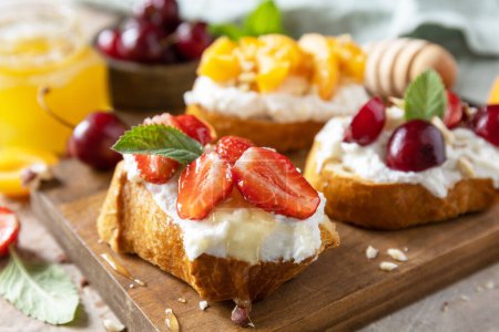 Photo for Berries toast breakfast, healthy food. Sandwich with cherry, strawberries, soft cheese and honey on wooden board on a stone  background. - Royalty Free Image