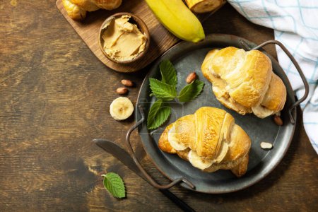 Photo for Healthy food dessert concept. French pastry. Tasty freshly baked croissants with peanut butter and banana on a rustic background. View from above. Copy space. - Royalty Free Image