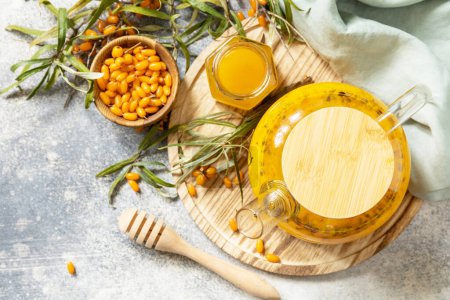 Foto de Té de espino amarillo saludable con miel sobre un fondo de piedra gris. Té de otoño, bayas bebida de temporada. - Imagen libre de derechos