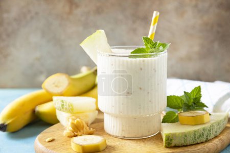 Photo for Banana smoothie with melon in drinking glass on wooden board on a stone background. Detox menu. Fresh seasonal smoothies. - Royalty Free Image