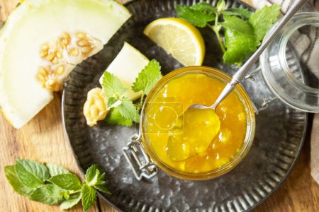 Photo for Homemade preserve. Sweet melon and citrus jam or jelly in small glass jar with fresh melon slices on wooden rustic table. View from above. - Royalty Free Image