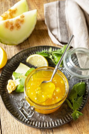 Photo for Homemade preserve. Sweet melon and citrus jam or jelly in small glass jar with fresh melon slices on wooden rustic table. - Royalty Free Image
