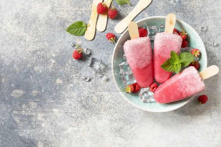 Téléchargez les photos : De la glace. Dessert d'été. Popsicles de framboises maison avec yaourt et framboises sur un fond de pierre grise. Vue d'en haut. Espace de copie. - en image libre de droit