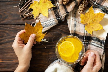 Photo for Seasonal autumn concept with drink. Cup of hot sea buckthorn tea with lemon, warm scarf and maple leaves on rustic background, creative flat lay. View from above. Copy space. - Royalty Free Image