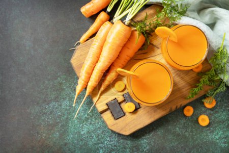 Photo for Carrot healthy juice for detox. Carrot juice in a glass and fresh carrots with leaves on a stone table. Healthy vegan vegetarian drink. View from above. Copy space. - Royalty Free Image