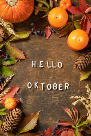 Photo for Hello oktober text, autumn season. Greeting card, fallen leaves, pumpkins and cones on a wooden board. Autumn natural background. View from above. - Royalty Free Image
