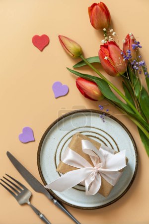 Photo for Beautiful table setting with  gift box, decorative hearts and tulips flowers on pastel peach background. Happy Mother's day concept background 2024. View from above. Empty space for text. - Royalty Free Image