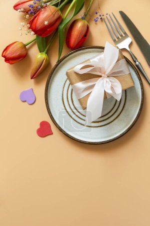 Photo for Beautiful table setting with  gift box, decorative hearts and tulips flowers on pastel peach background. Happy Mother's day concept background 2024. View from above. Empty space for text. - Royalty Free Image