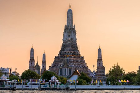 Téléchargez les photos : Wat Arun stupa, ou le temple de l'aube, un point de repère important de Bangkok, Thaïlande, se dresse bien en vue le long de la rivière Chao Phraya, avec un beau ciel orange coucher de soleil. - en image libre de droit
