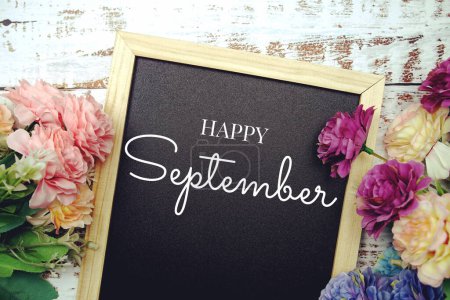Happy September Text auf schwarzem Grund mit Blumenstrauß auf hölzernem Hintergrund dekoriert