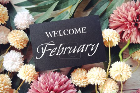 Welcome February text message with flower decoration on wooden background