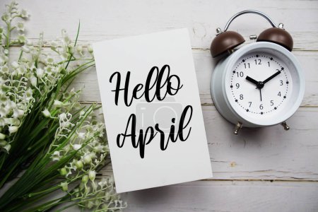 Hello April text message with flower and alarm clock on wooden background